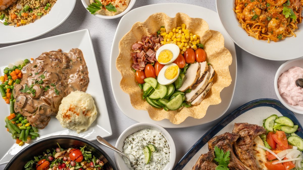 A spread of dishes from the Syn Tois Allois kitchen: lamb chops, a salad bowl, prawn pasta, steak with mushroom sauce and dips